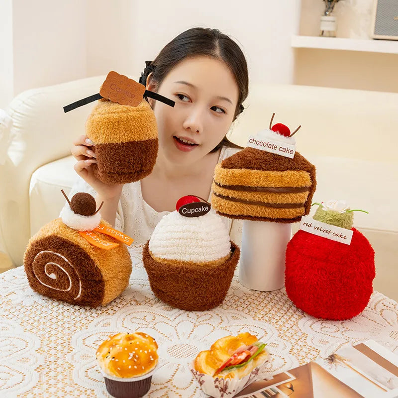 Woman holding plush toy cakes resembling different desserts on a table.