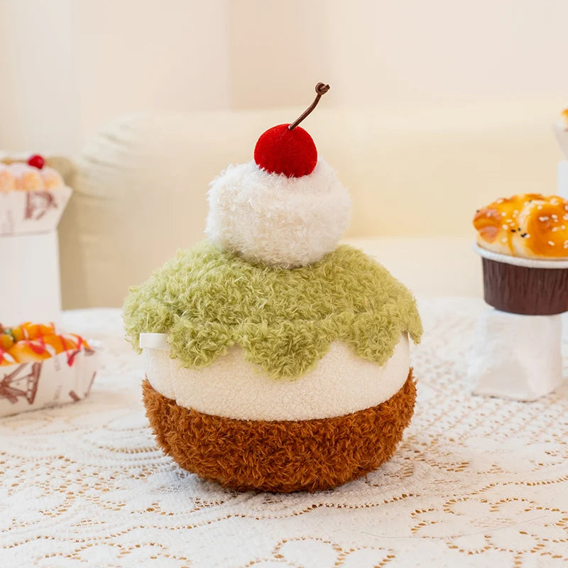 Plush toy resembling a layered dessert with a cherry on top on a lace tablecloth.