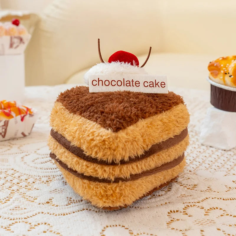 Plush toy resembling a chocolate cake with a cherry on top, labeled 'chocolate cake', on a lace tablecloth.