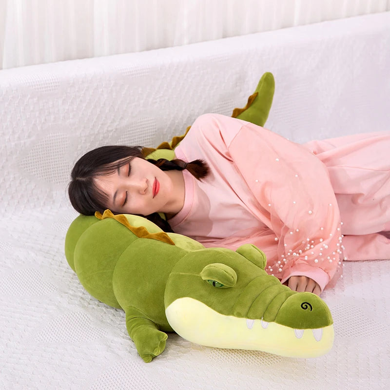 Person lying on a large green crocodile-shaped body pillow on a white couch.