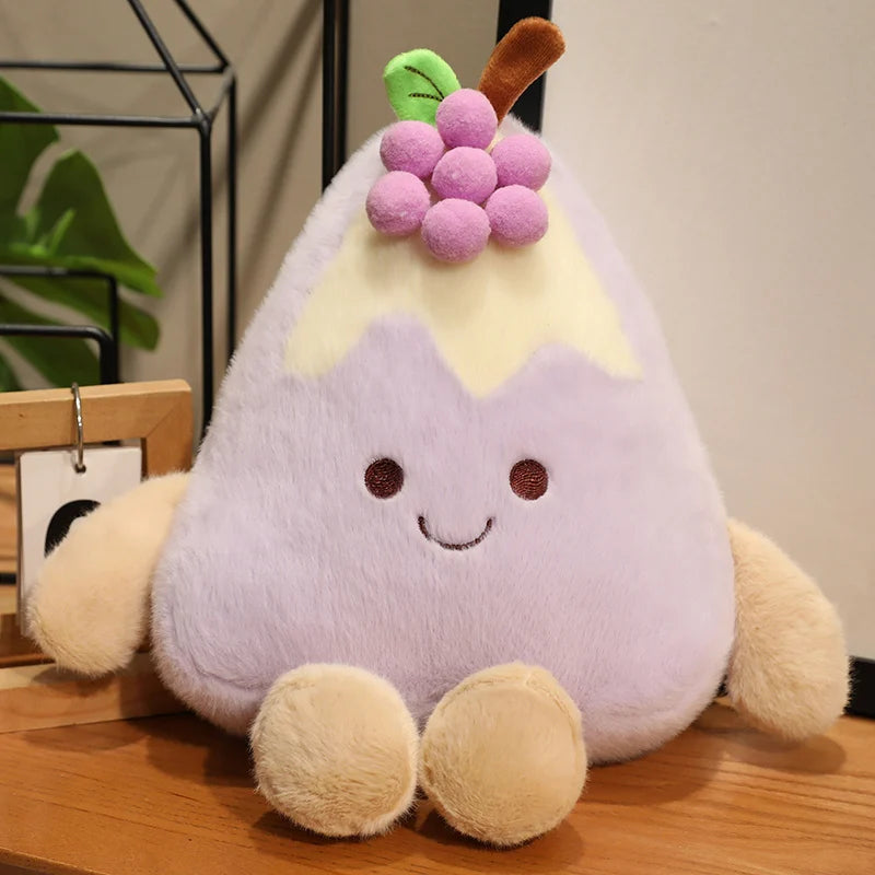 Plush toy shaped like a cake slice with a purple body, yellow top, and pink grapes on a wooden surface.