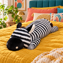 Long black-and-white striped zebra plush body pillow with a rounded black muzzle, brown mane, gray hooves and striped tail displayed across a mustard-yellow bed in a colorful bedroom.