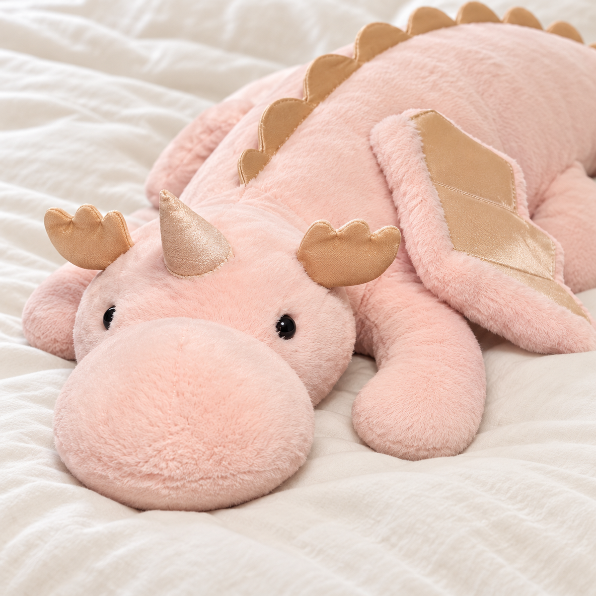 Close-up of the pink Cuddle Soft dragon plushie's soft muzzle, small horn, beige ear fins, stitched wing, and short-pile fabric.