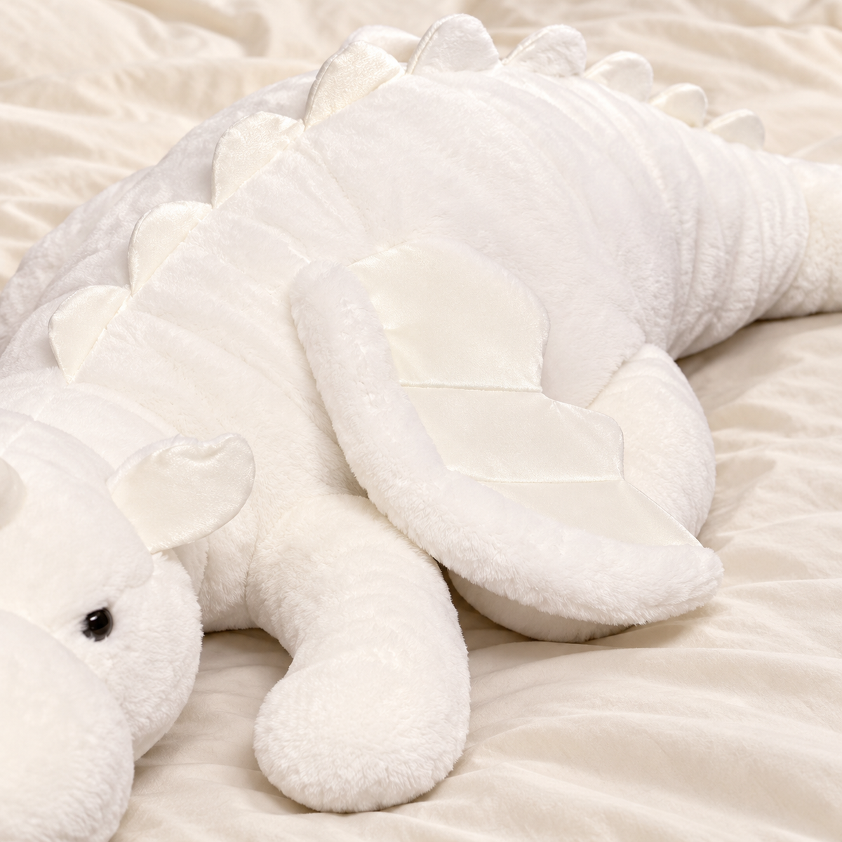 Close-up of the white Cuddle Soft dragon plushie's pale fabric wing, soft dorsal spikes, and plush body texture.