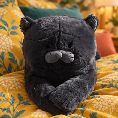 Close-up of the black cat plush pillow’s rounded face, small ribbed ears, low sleepy eyes, central brow seam, gray double-lobed muzzle, round gray nose, whisker stitching, and velvety fabric.