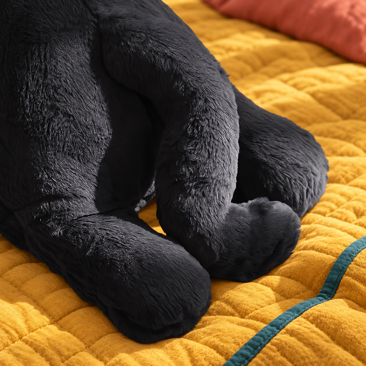 Close-up of the Moonlight Black Cat Body Pillow’s extended front paws, rounded rear paw, curved tail, visible seams, and soft charcoal-black plush construction on mustard bedding.
