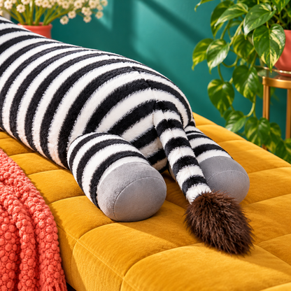 Rear close-up of the striped zebra plush body pillow showing two gray hooves, black-and-white striped tail with a brown tuft, and stitched seams on a mustard bench.