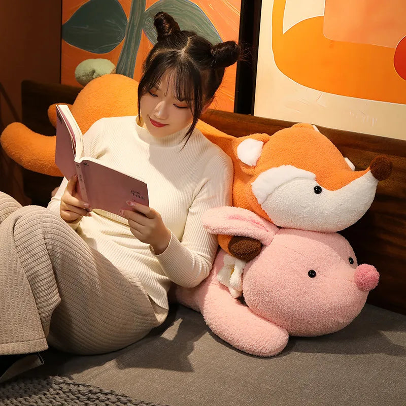Woman reading a book next to two large plush toys, one orange and one pink, against a colorful wall.