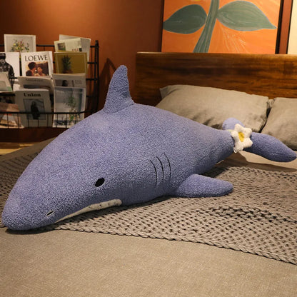 Blue shark-shaped plushie body pillow on a bed with a magazine rack and painting in the background