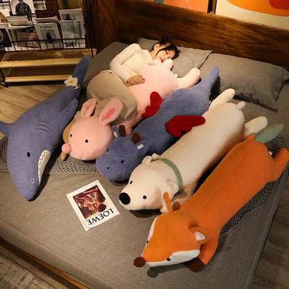 Person lying on a bed with large plush toys shaped like animals, including a shark, rabbit, hippo, polar bear, and fox.