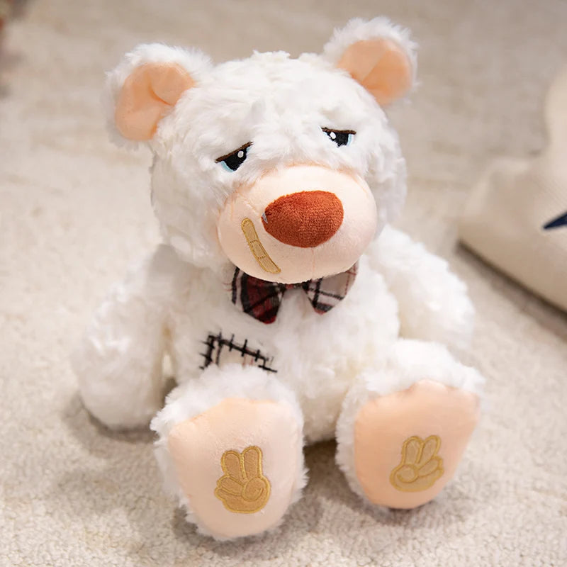 White teddy bear with a bow tie and band aid sitting on a carpeted floor.