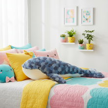 Colorful bedroom with a bed featuring shark-shaped plushie and a shelf with plants.