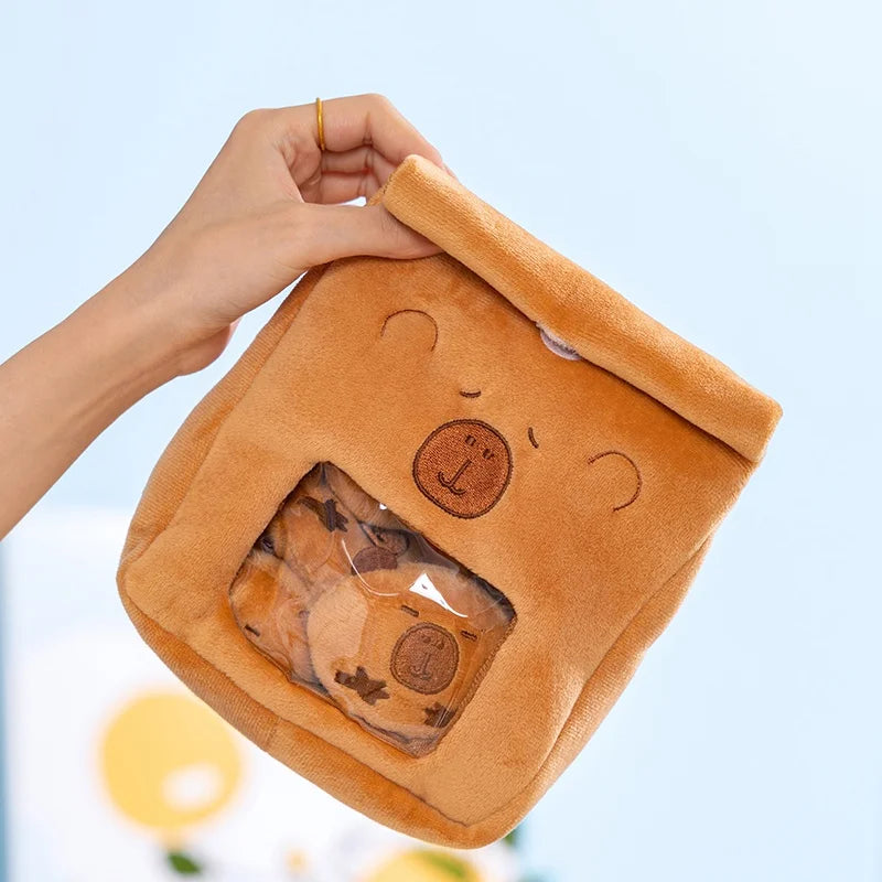 Brown capybara pudding bag plush toy with a face design held by a hand against a light blue background