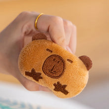 Hand holding a small brown capybara plush toy with a face on a blurred background