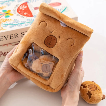 Brown capybara plush toy with a clear window showing a smaller plush toy inside, held by a hand.
