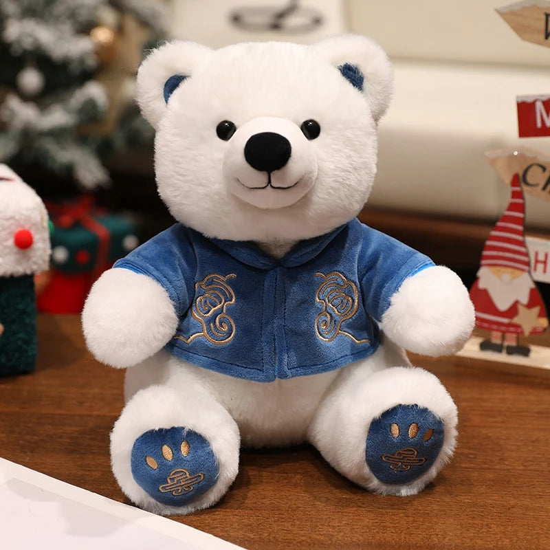 White teddy bear with a blue jacket on a wooden surface with Christmas decorations in the background.