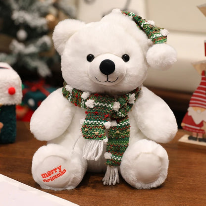 White teddy bear wearing a green and red scarf with 'merry christmas' text, sitting on a wooden surface.