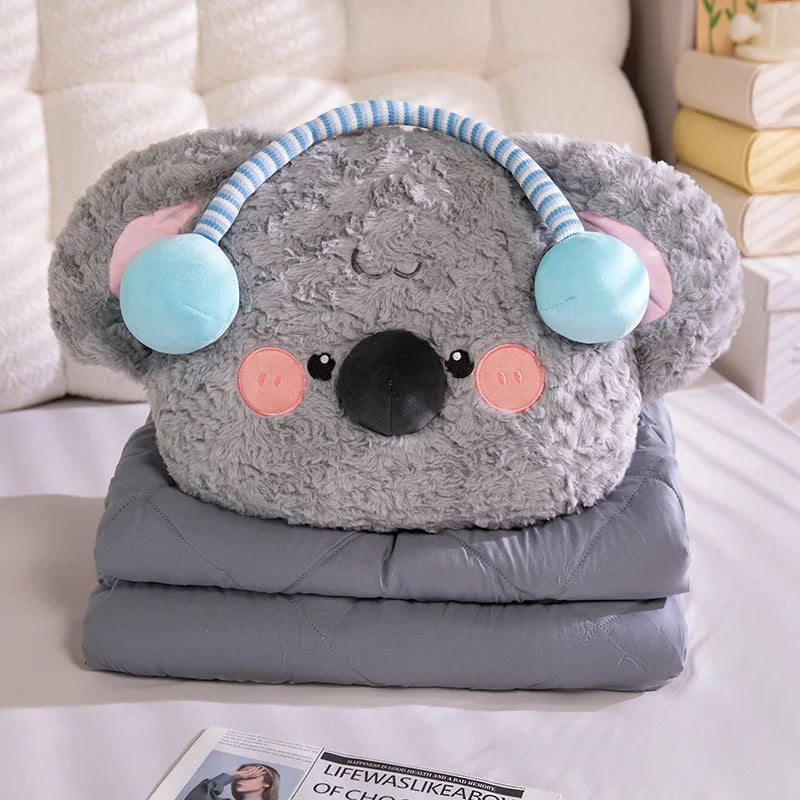 Gray koala-shaped pillow with pink ears and blue pom-poms on a white surface.