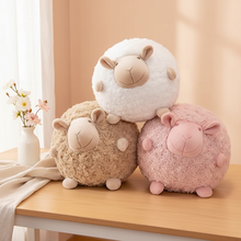 Three fluffy sheep plush toys in white, beige, and pink on a wooden surface with a light background.