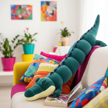 Dark green Crocodile Long Plushie Body Pillow on a sofa next to a book in a bright living room setting