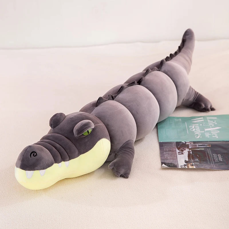 Gray crocodile plushie body pillow on a bed with a magazine underneath