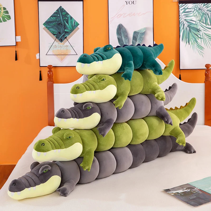 Stack of green and gray crocodile plushie body pillows on a bed with a colorful wall in the background.