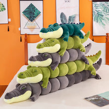 Stack of green and gray crocodile plushie body pillows on a bed with a colorful wall in the background.