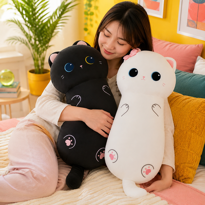 A woman sitting on a bed holds two large cat-shaped plush toys, one black and one white, in a brightly lit bedroom setting.