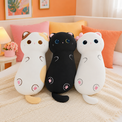 Three cute cat-shaped plush pillows in white, black, and calico are arranged together on a cozy cream-colored bed with pink and orange pillows in the background.