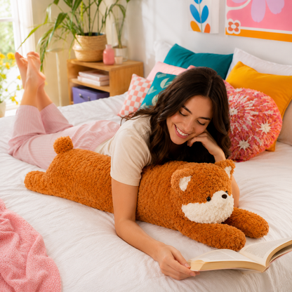 A woman lies on a bed reading a book while holding a large, fluffy orange fox plush toy with a white snout and ears. The bedroom is brightly lit with colorful pillows, a wooden side table, and houseplants in the background.