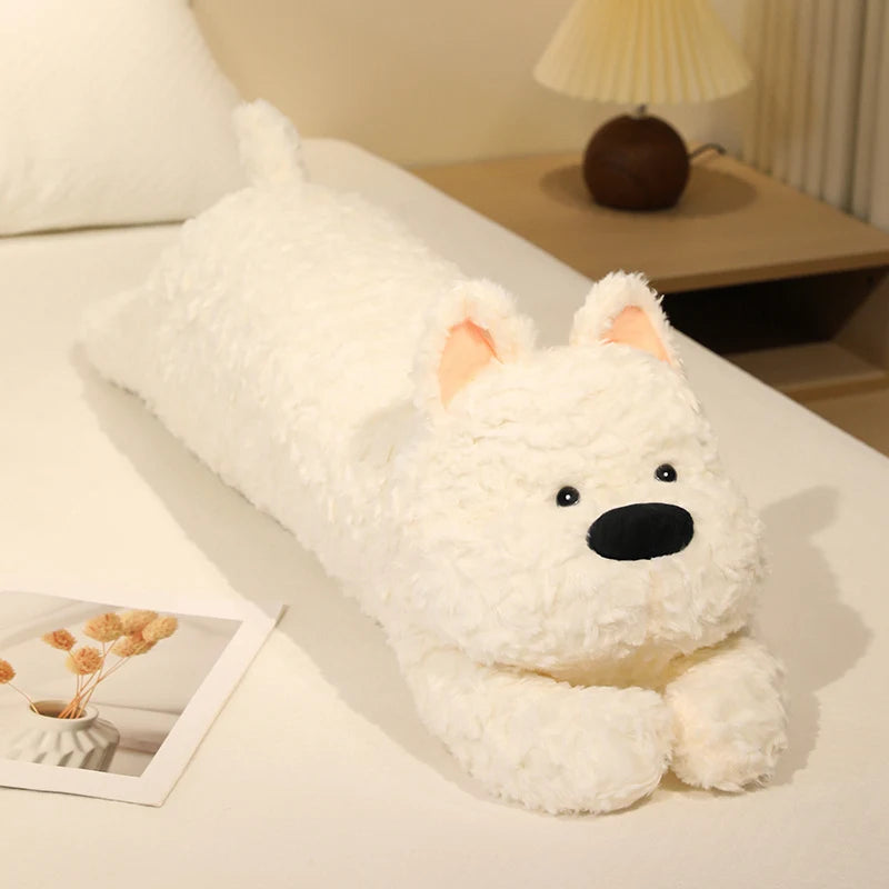 White plush dog toy on a bed with a lamp and decor in the background