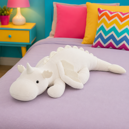 A white plush dragon toy with small horns and wings lies on a lavender bed in a colorful bedroom. Bright pink, yellow, and chevron-patterned pillows are visible behind it, along with a turquoise side table and lamp.