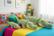 Green alligator plush toys on a colorful bed with decorative pillows and plants in the background.