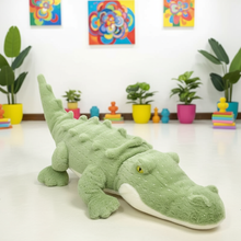 Green plush alligator toy on a white floor with colorful plants and toys in the background