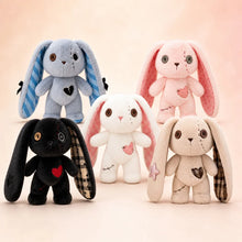 Four plush bunny toys arranged together on a soft peach background. The bunnies are light blue with blue plaid ears, light pink with pink plaid ears, black with plaid ears and a red heart, and cream with plaid ears and a pink star.