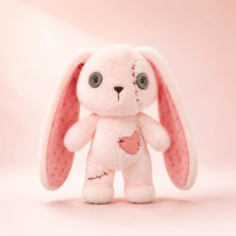 A pink plush bunny toy with long floppy ears, gray button eyes, and a small stitched heart on its chest, centered on a soft pink background.