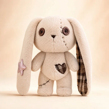 A handmade plush bunny toy with long floppy ears, one ear showing a brown plaid lining, a pink glitter star on one ear, and a brown plaid heart patch on the chest, set against a warm beige background.
