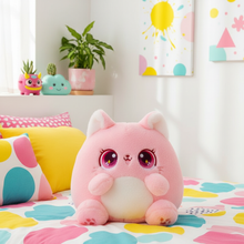 Pink plush cat with large eyes on a colorful bedspread in a room with decorative elements.