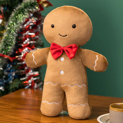Plush gingerbread man toy with a red bow tie in front of a decorated Christmas tree.