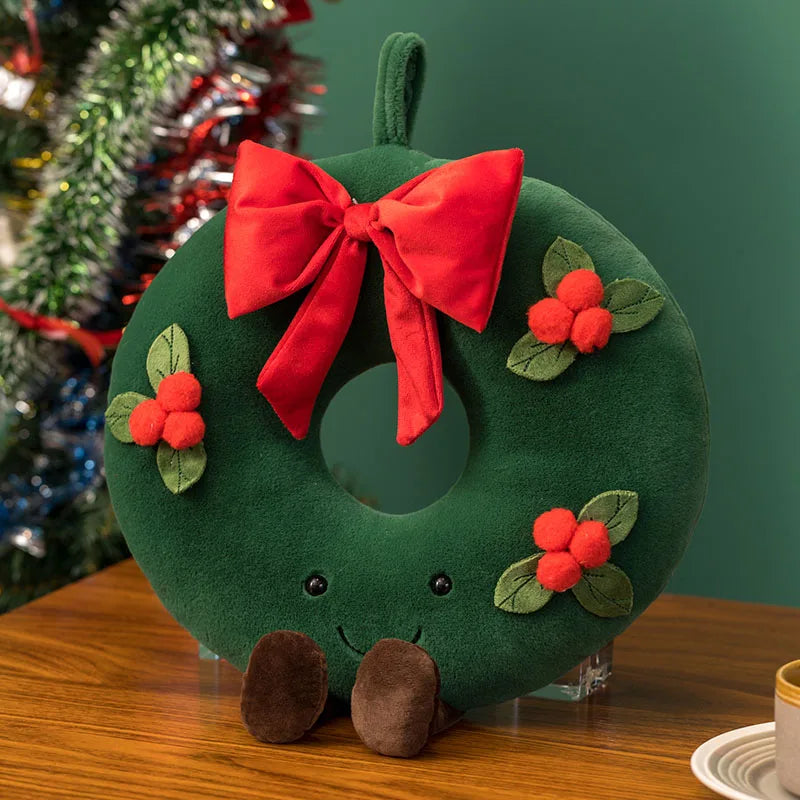 Green plush wreath with a red bow and holly leaves on a wooden surface.