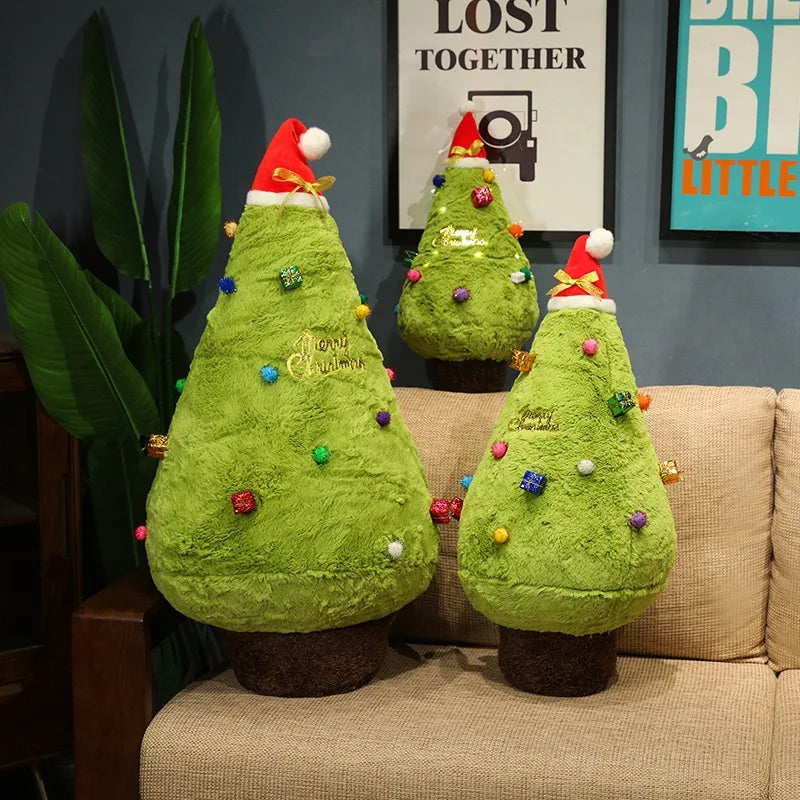Three green Christmas tree-shaped plushies with colorful decorations on a beige couch.
