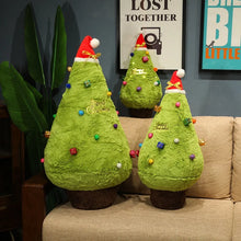 Three green Christmas tree-shaped plushies with colorful decorations on a beige couch.