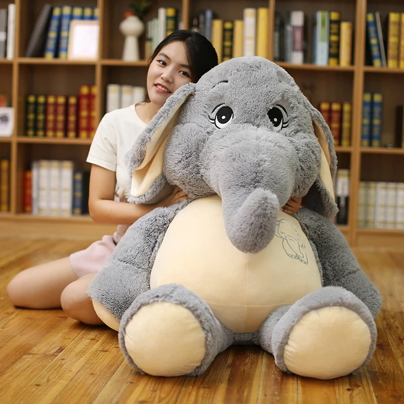Person holding a large gray elephant plush toy in a room with bookshelves.