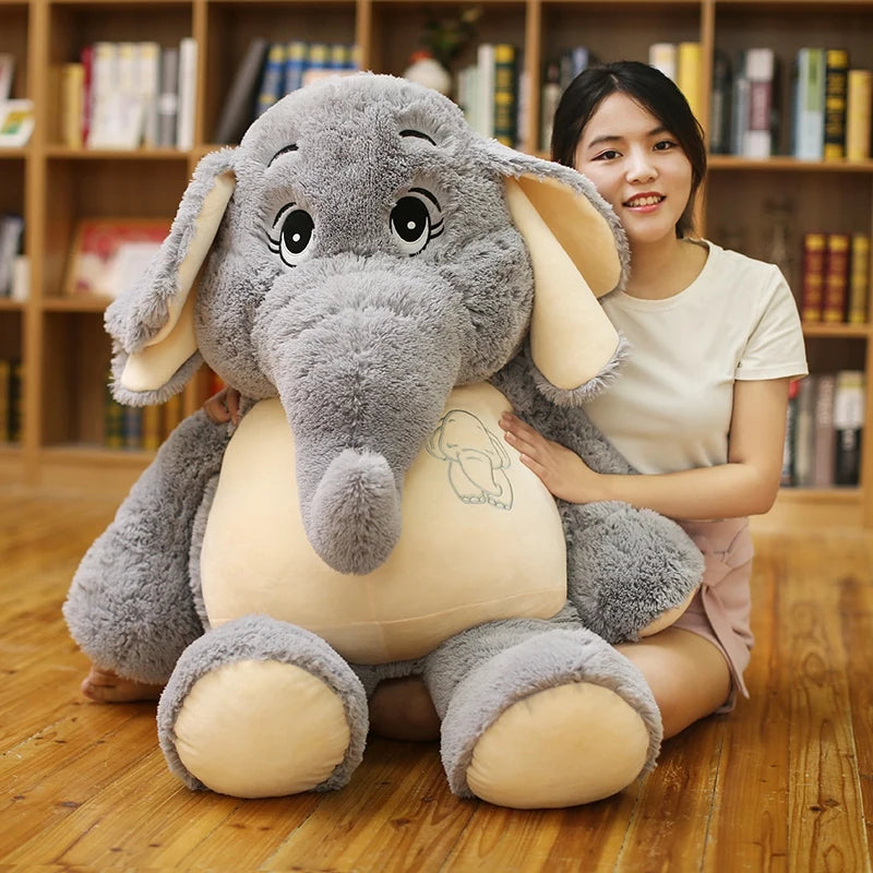 Person holding a large plush elephant toy in a room with bookshelves.