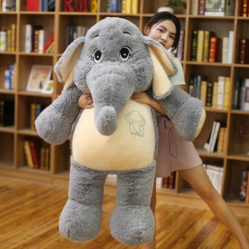 Person holding a large plush elephant toy in a room with bookshelves.