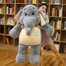 Person holding a large plush elephant toy in a room with bookshelves.