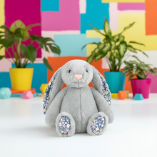 Gray plush bunny with floral patterns on a colorful geometric background