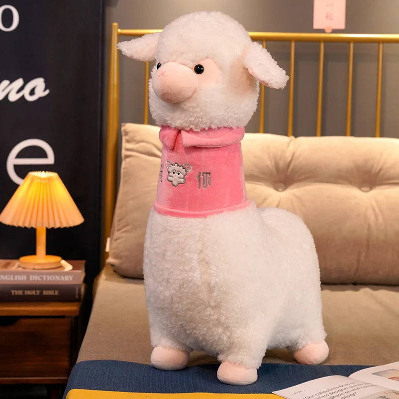 Plush toy sheep wearing a pink sweater on a couch with a lamp and books in the background.