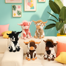 Four plush cow toys in different color and pattern designs arranged on a cream-colored sofa in a brightly lit room with a mint green wall, framed art, and a potted plant.