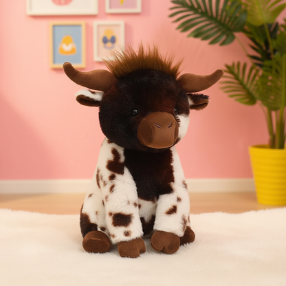 A plush toy highland cow sitting on a white rug in a pink room with framed pictures and a potted plant in the background.